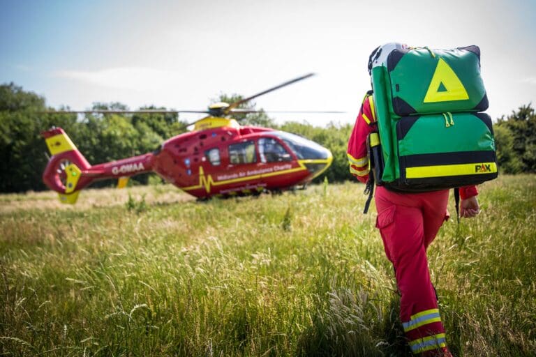 The Midlands Air Ambulance Charity helicopter landing in a field with a critical care paramedic walking towards the helicopter with a packed, green medical bag.