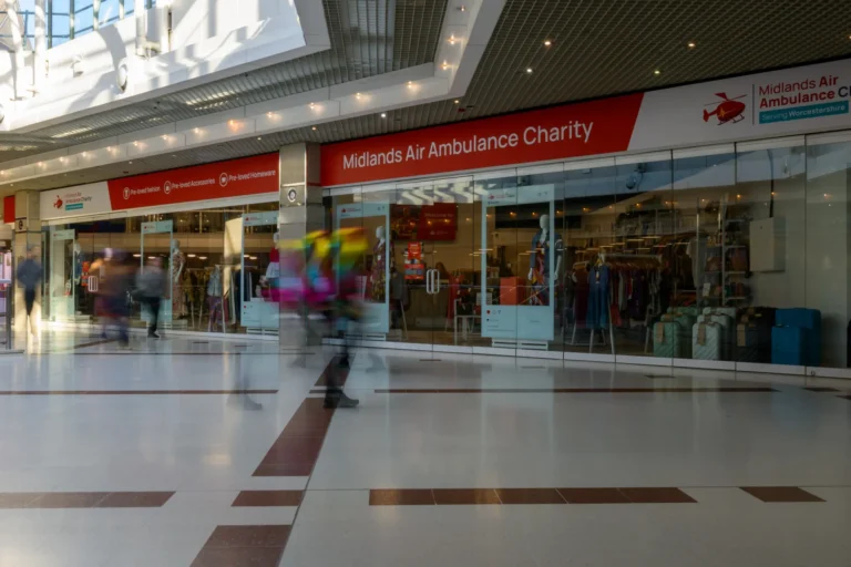 The front of Midlands Air Ambulance charity shop in Worcester with a person with a blurred out effect walking in front of the shop.