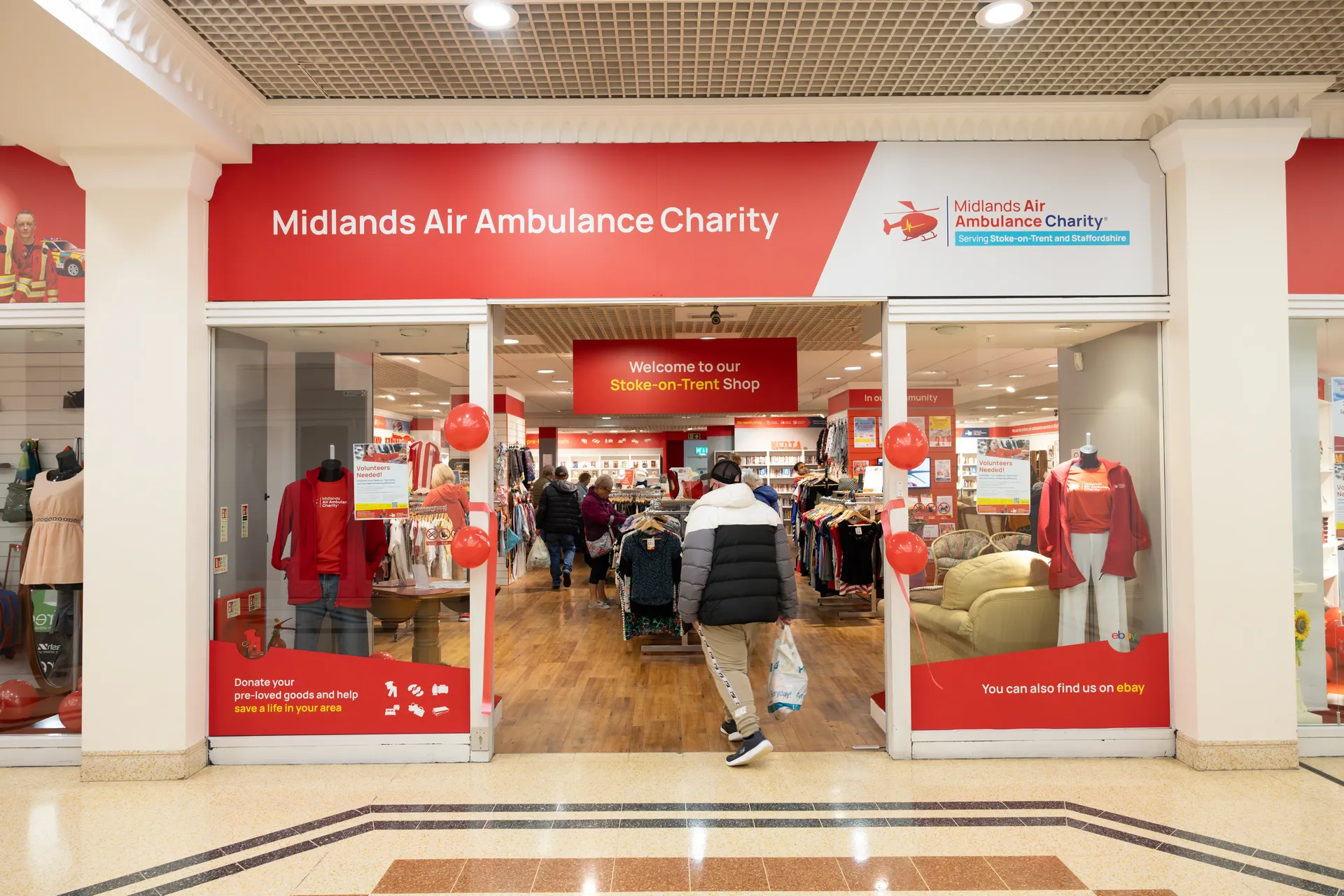 The front window display of Midlands Air Ambulance Charity Shop in Stoke-On-Trent, with a male in a black jacket walking into the store.
