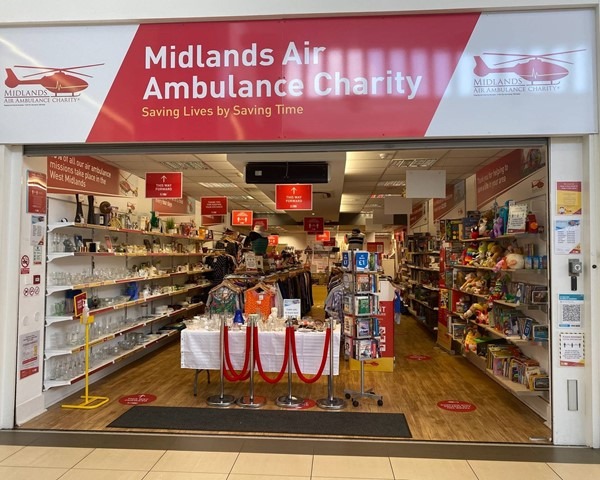 The front of Midlands Air Ambulance charity shop in West Bromwich with bright red signage and a table display in the window.