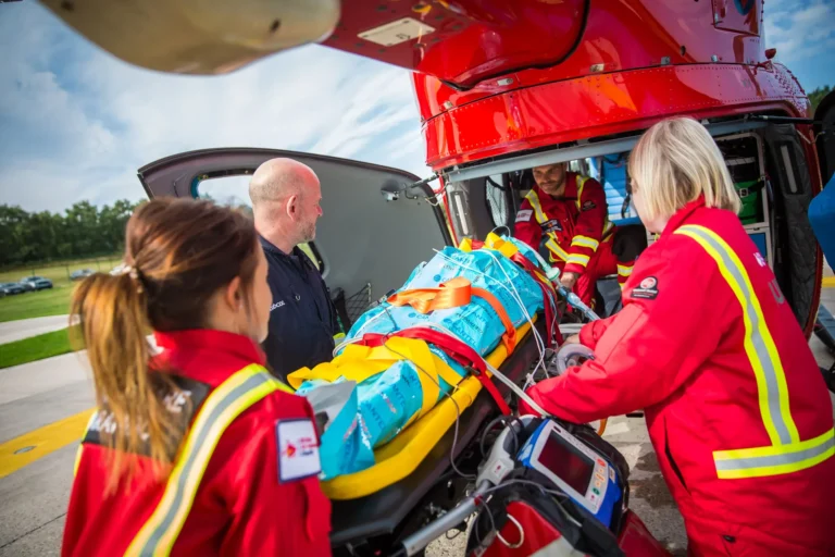 Three Air Ambulance crew members loading a patient wrapped in a blue, thermal cover onto the helicopter.