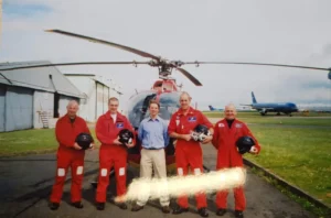 Maac Crew Of Men In Red Uniforms Standing In Front Of A Helicopter