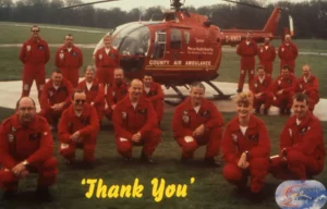 Maac Group Of Men In Red Uniforms Posing In Front Of A Helicopter