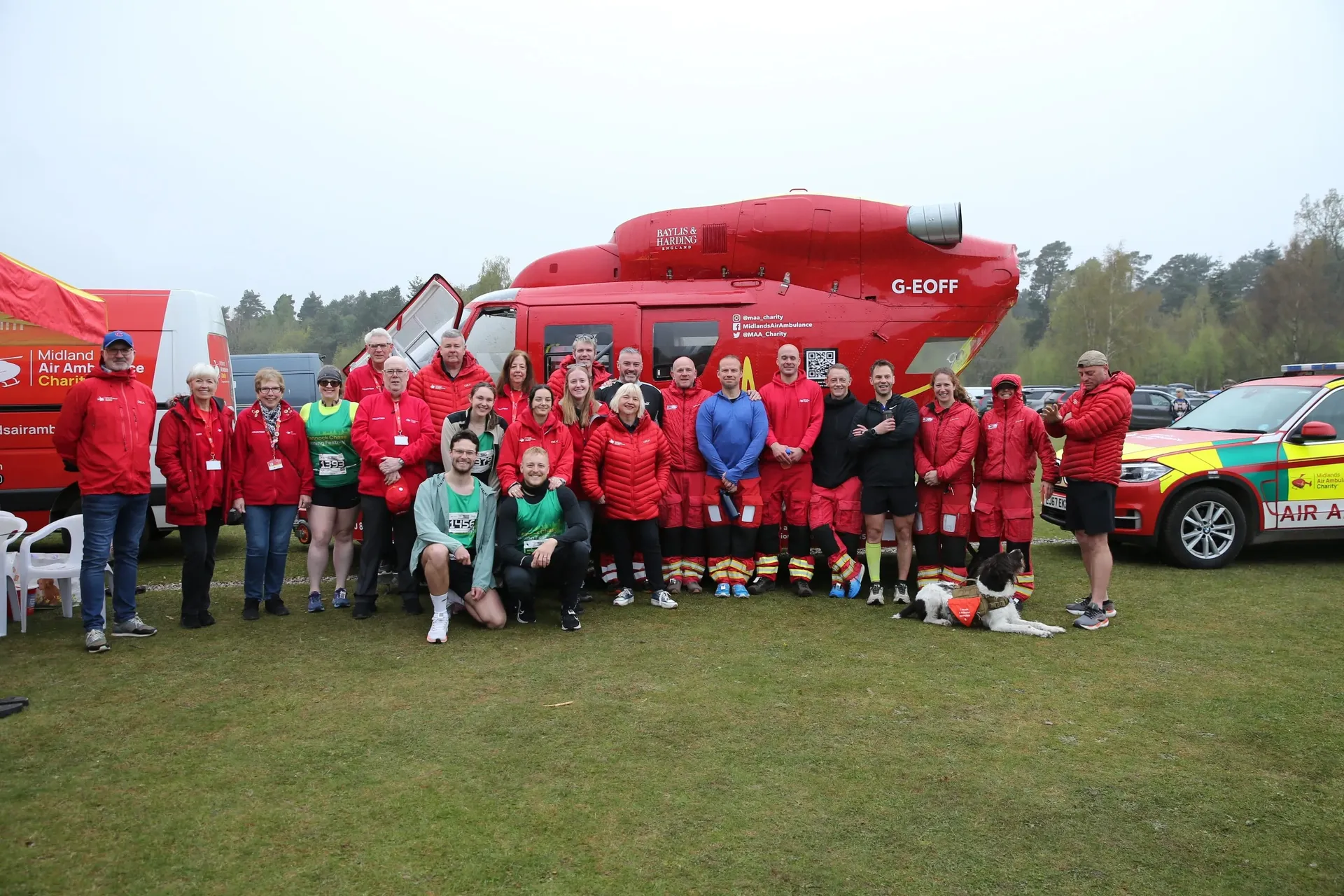 Maac Group Of People In Red Jackets Standing In Front Of A Red Helicopter