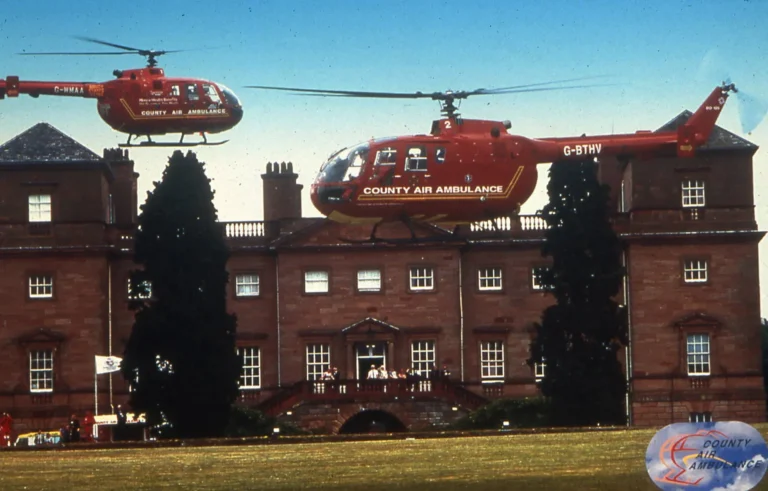 Maac Helicopters Flying Over A Large Building With A Clock Tower