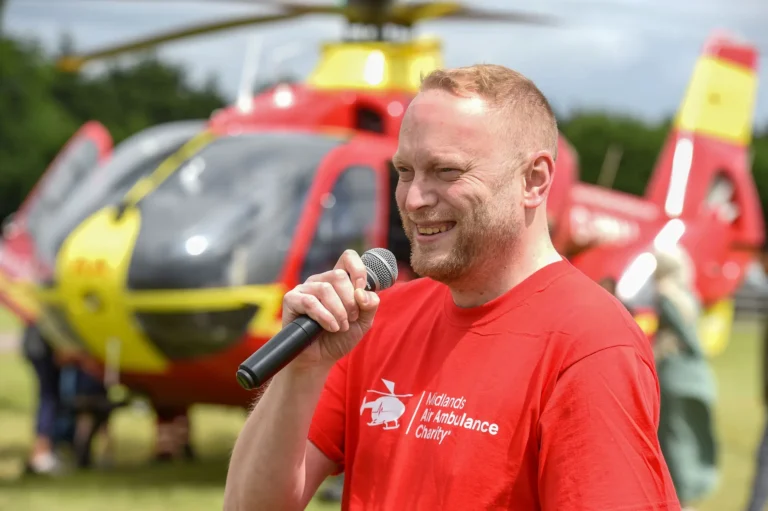Maac Man In Red Shirt Holding A Microphone In Front Of A Helicopter