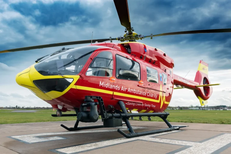 Maac Red Helicopter Sitting On A Runway With A Cloudy Sky