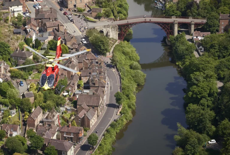 A Midlands Air Ambulance helicopter flying over Shropshire, with a river in the aerial view.