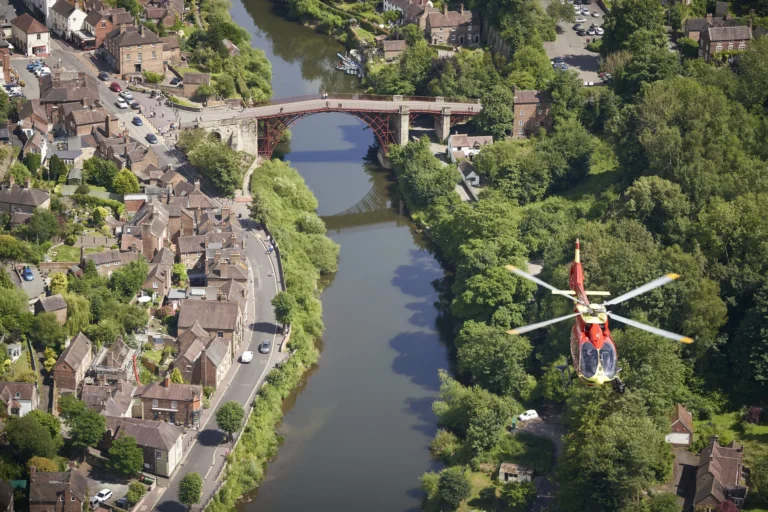 Maac Shropshire Arafed Helicopter Flying Over A River With A Bridge In The Background