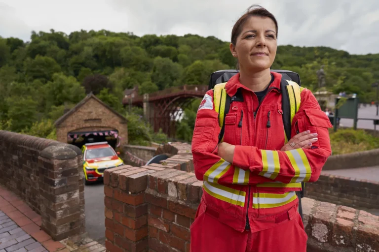Maac Shropshire There Is A Woman In A Red Fire Suit Standing In Front Of A Car