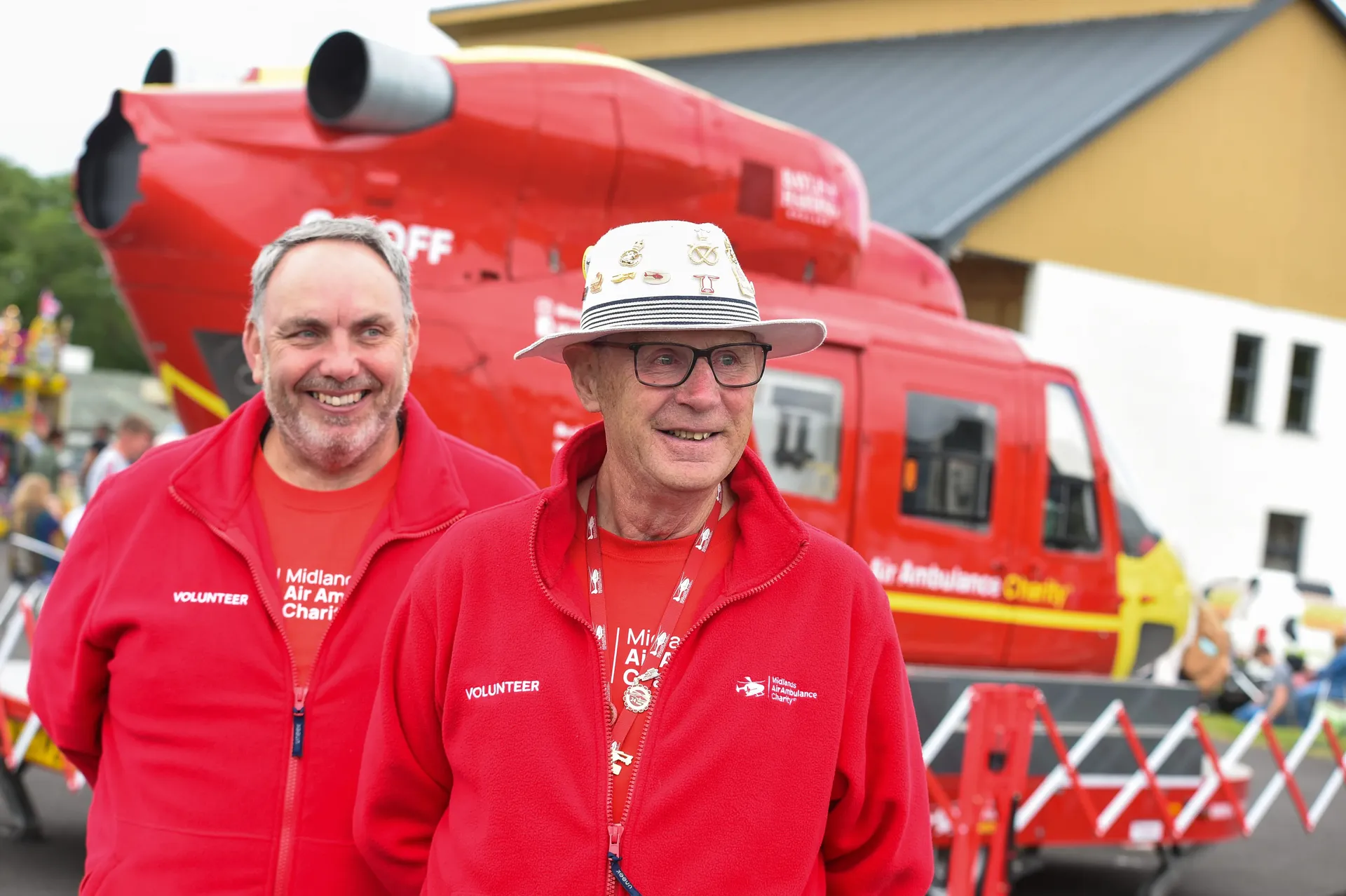 Maac They Are Two Men Standing In Front Of A Red Helicopter