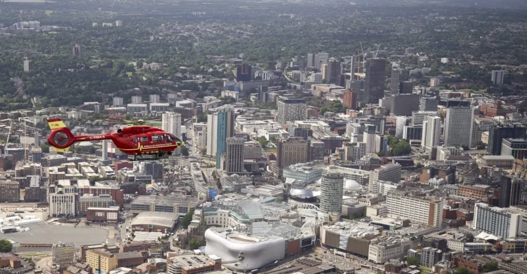 A Midlands Air Ambulance helicopter flying over the busy, cityscape of the West Midlands.