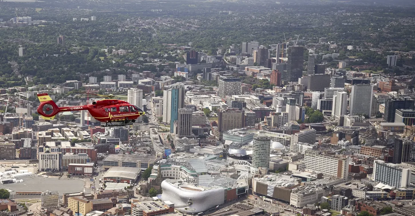 A Midlands Air Ambulance helicopter flying over the busy, cityscape of the West Midlands.