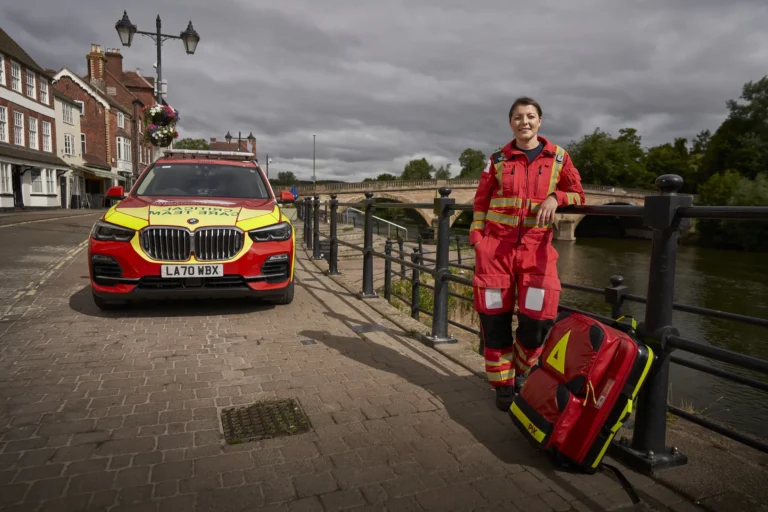 Maac Worcesteshire Woman In Red And Yellow Uniform Standing Next To A Car