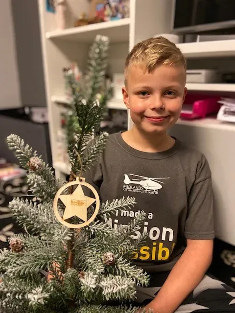 Maac Boy Sitting In Front Of A Christmas Tree With A Star Ornament