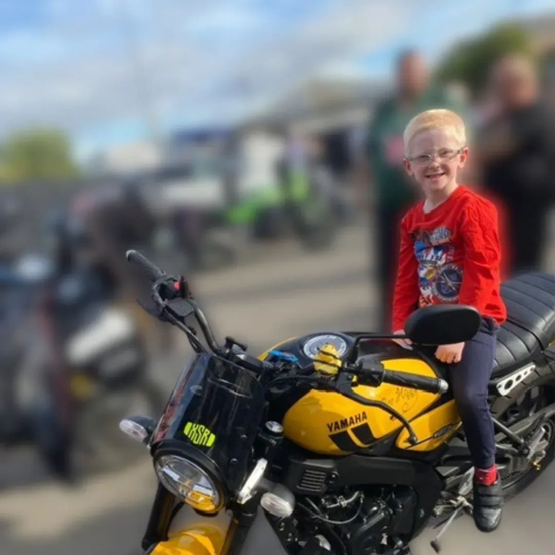 Maac Boy Sitting On A Yellow Motorcycle In A Parking Lot