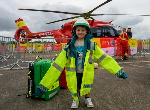 Maac Child In Safety Gear Standing In Front Of A Helicopter