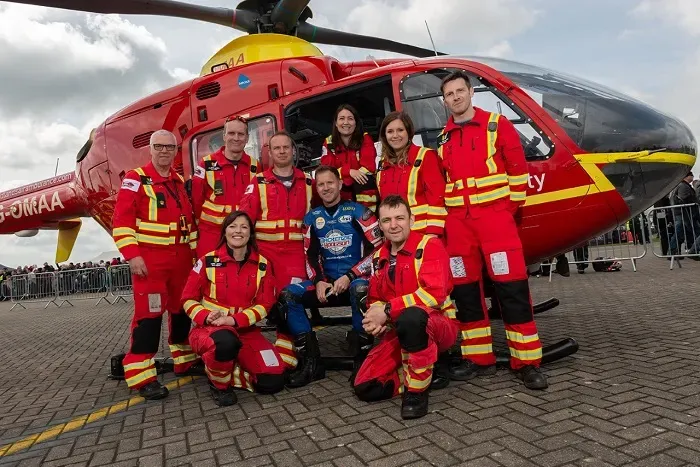 Maac Crew Of People In Red Uniforms Posing In Front Of A Helicopter