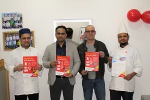 Maac Four Men Holding Up Red And White Cookbooks In A Room