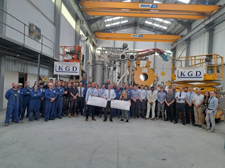 Maac Group Of Men Standing In A Factory Holding A Check