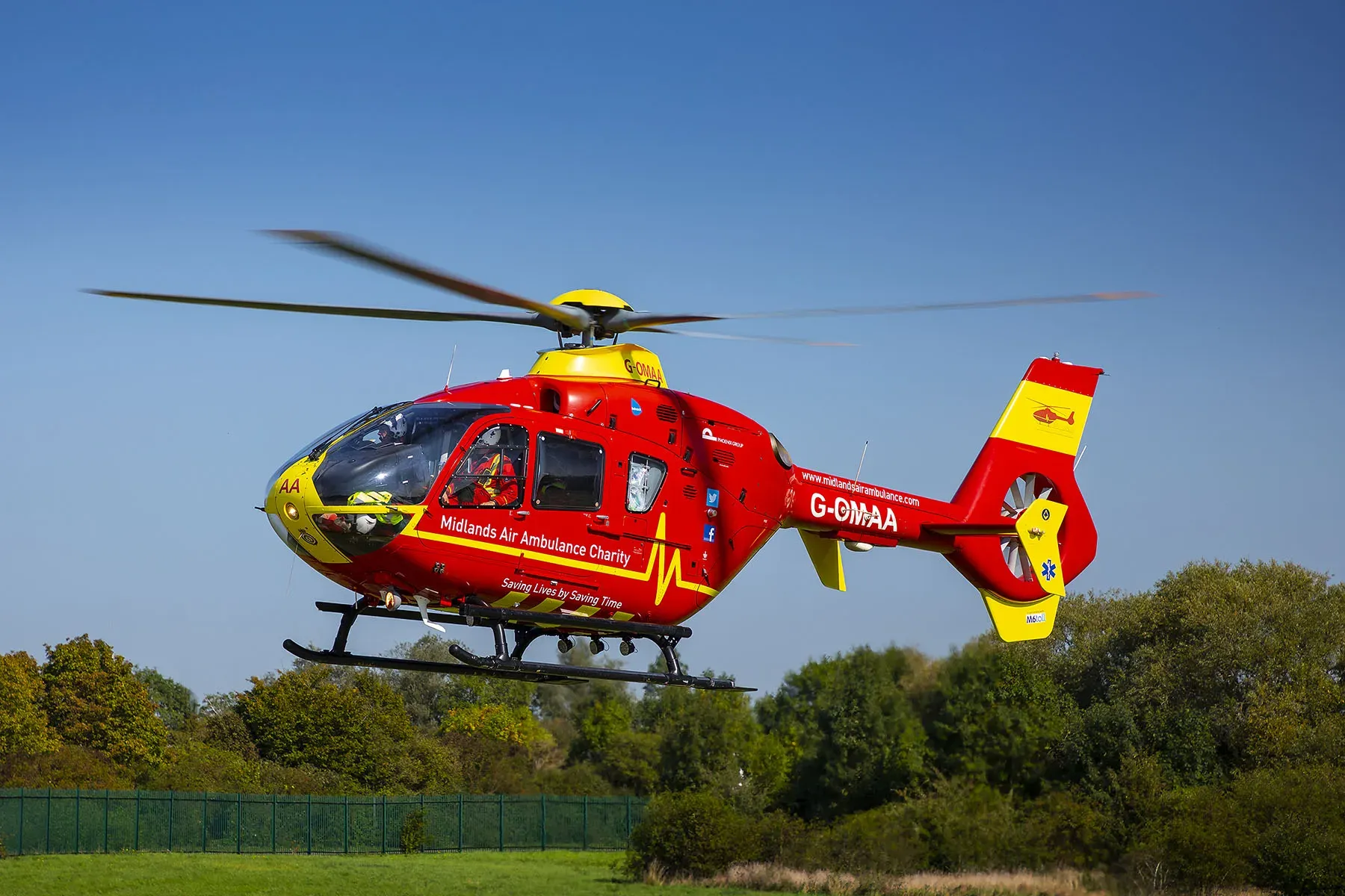 Maac Helicopter Flying Low Over A Field With Trees In The Background
