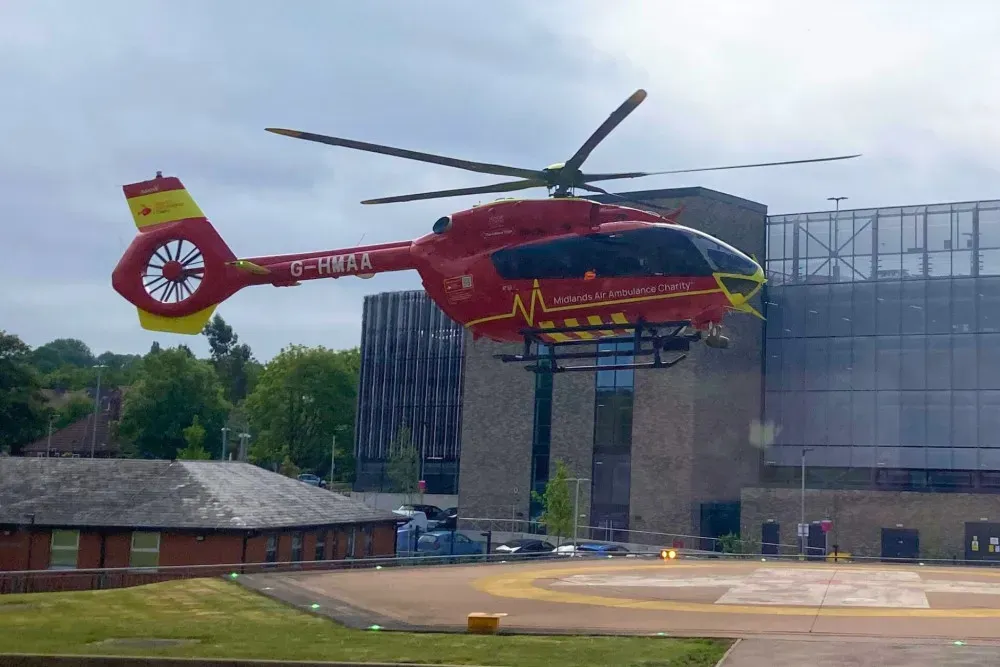 Maac Helicopter Flying Over A Building With A Large Building In The Background