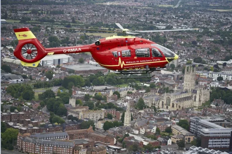 Maac Helicopter Flying Over A City With A Church In The Background