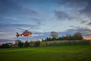 Maac Helicopter Flying Over A Field With A Sunset In The Background