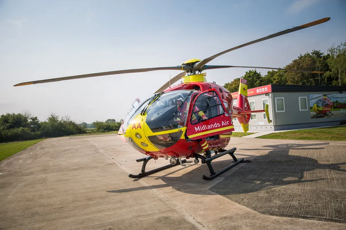 Maac Helicopter Parked On A Runway With A Man Standing Next To It