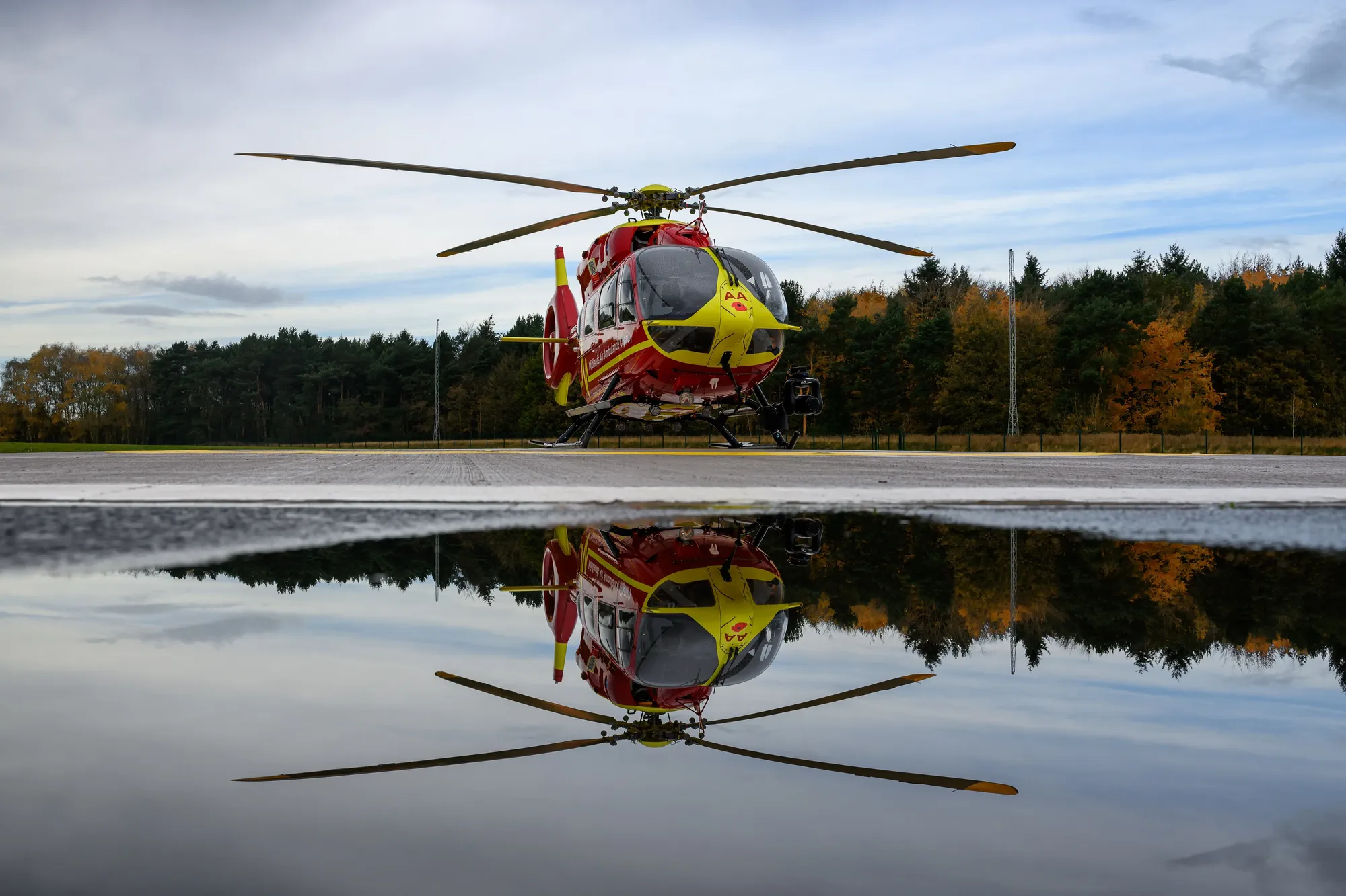 Maac Helicopter Sitting On The Tarmac With Its Reflection In The Water