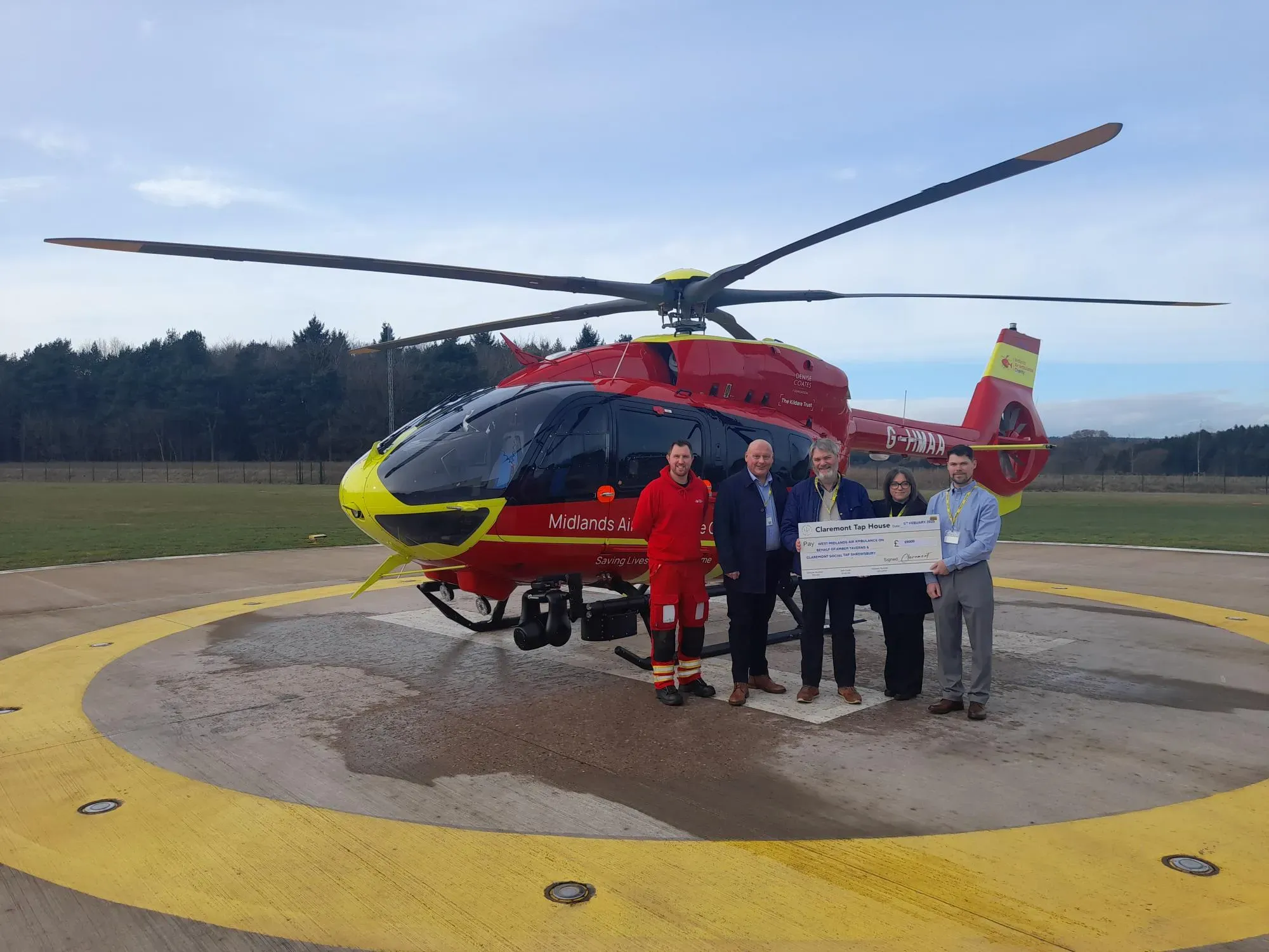 Maac Helicopter With A Man Holding A Check Standing Next To A Man And A Woman