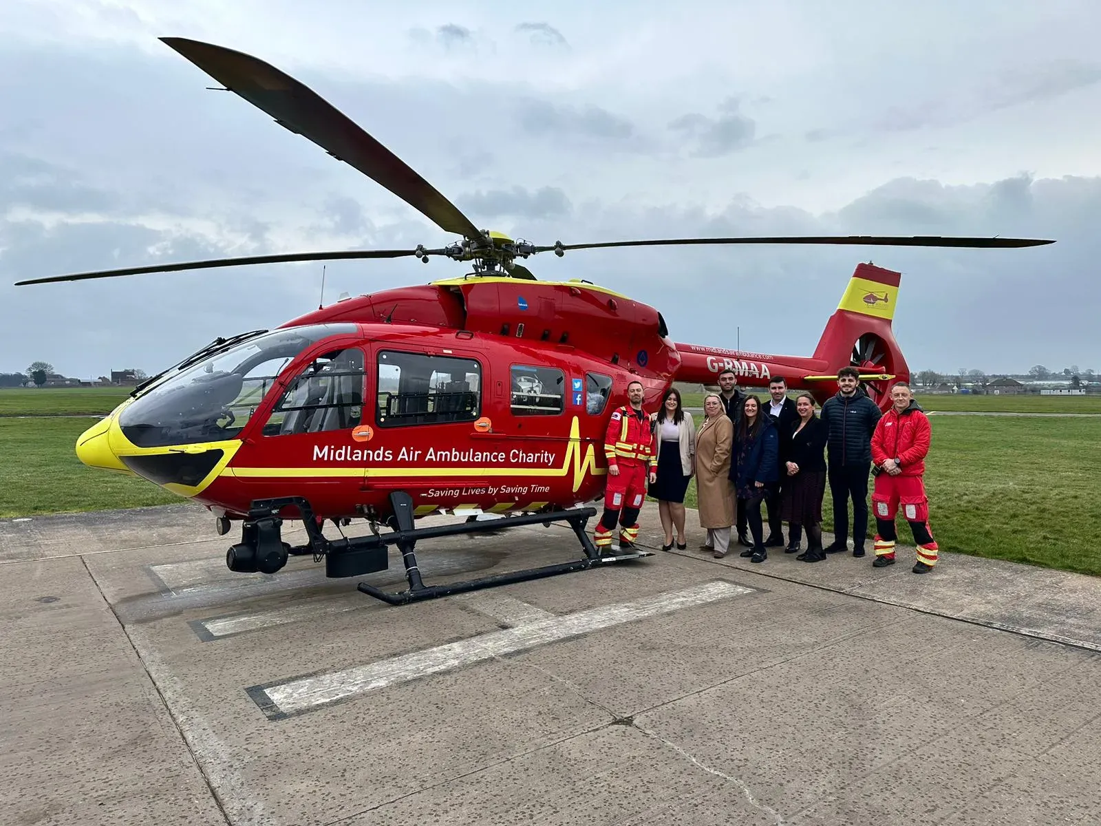 Maac Helicopter With People Standing In Front Of It On A Runway