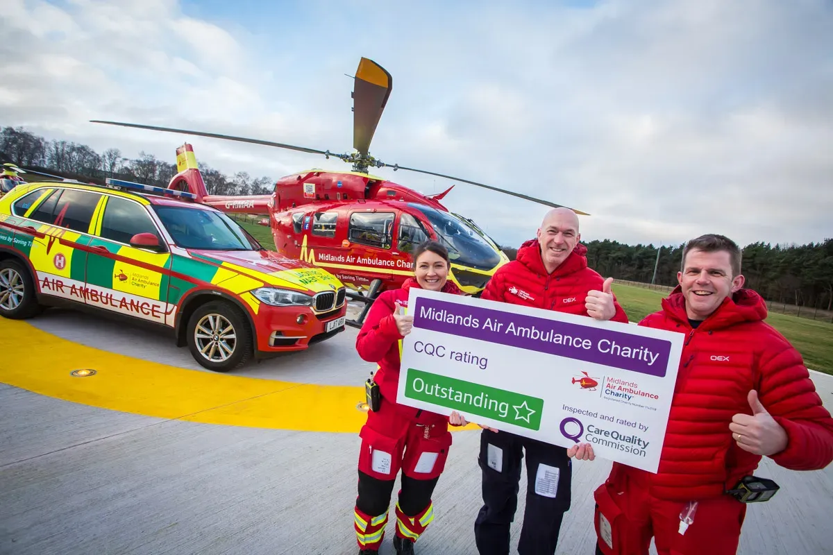 Maac Man And Woman Holding A Cheque And A Car With A Helicopter In The Background