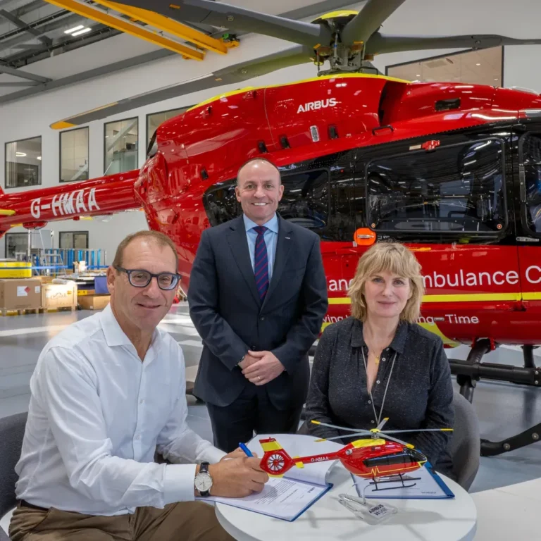 Maac Man And Woman Sitting At A Table In Front Of A Helicopter