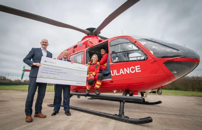 Maac Man And Woman Standing In Front Of A Helicopter Holding A Check