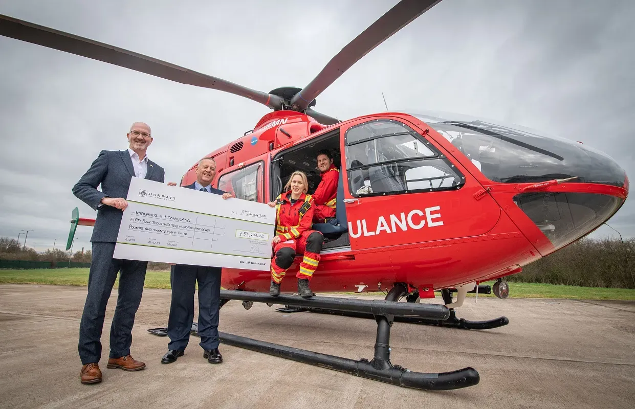 Maac Man And Woman Standing In Front Of A Helicopter Holding A Check
