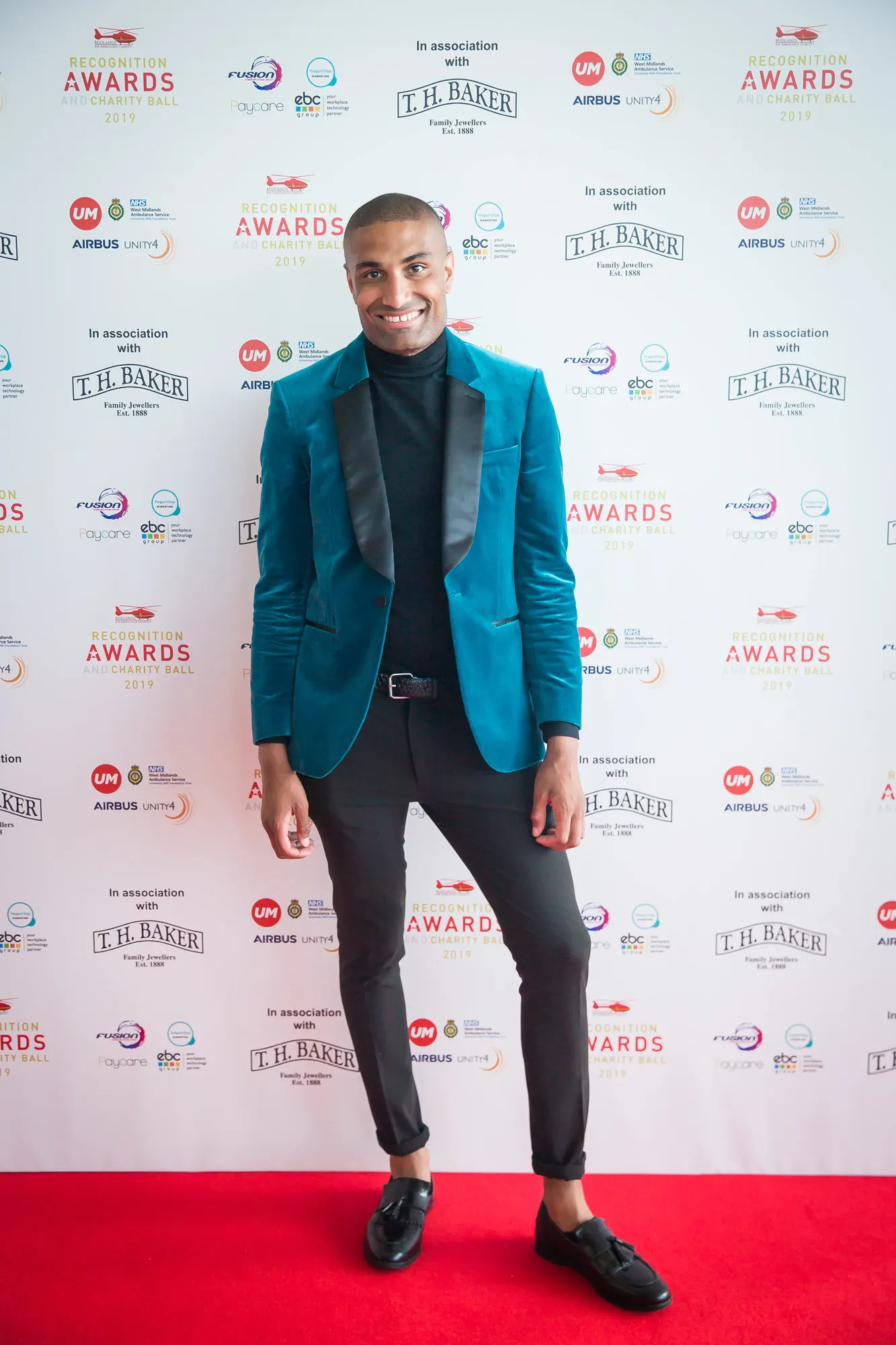 Maac Man In A Blue Suit And Black Shirt Standing On A Red Carpet