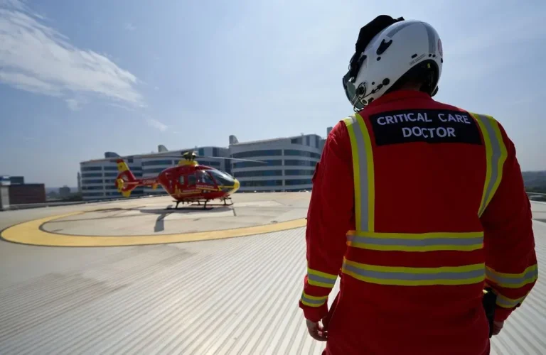 Maac Man In A Red Uniform Standing In Front Of A Helicopter