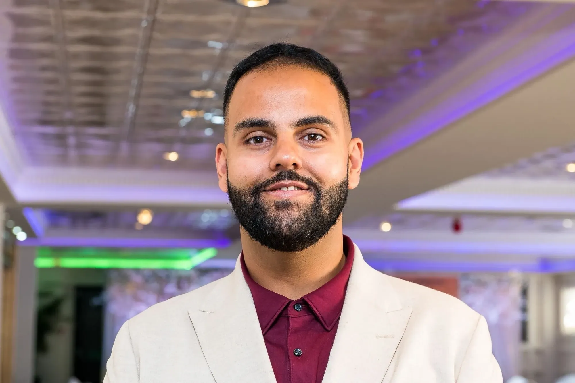 Maac Man In A White Suit And Maroon Shirt Smiling
