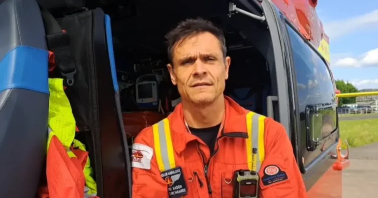 Maac Man In An Orange Jacket Standing In Front Of A Helicopter