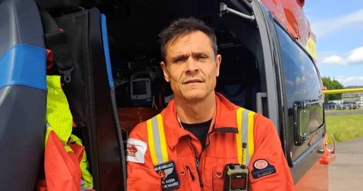 Maac Man In An Orange Jacket Standing In Front Of A Helicopter