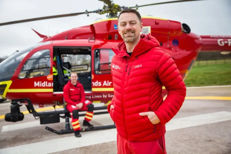 Maac Man In Red Jacket Standing In Front Of A Helicopter