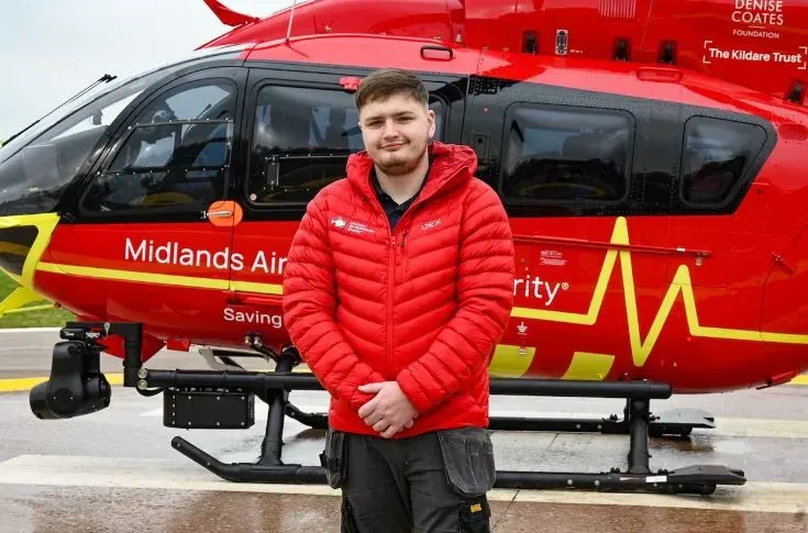 Maac Man In Red Jacket Standing In Front Of A Red Helicopter