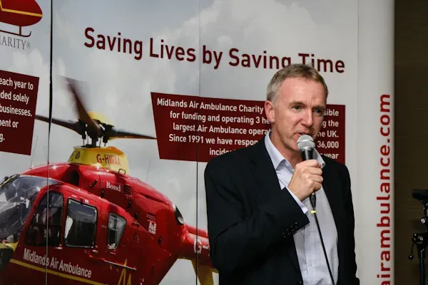 Maac Man Speaking Into A Microphone In Front Of A Poster