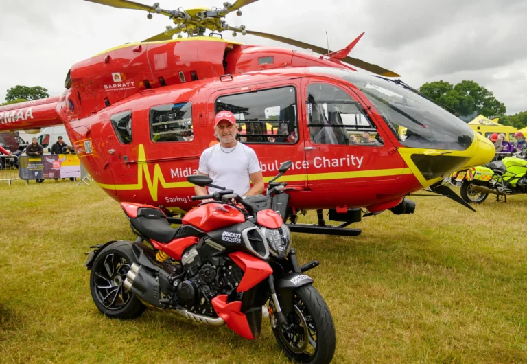 Maac Man Standing Next To A Red Motorcycle In Front Of A Helicopter