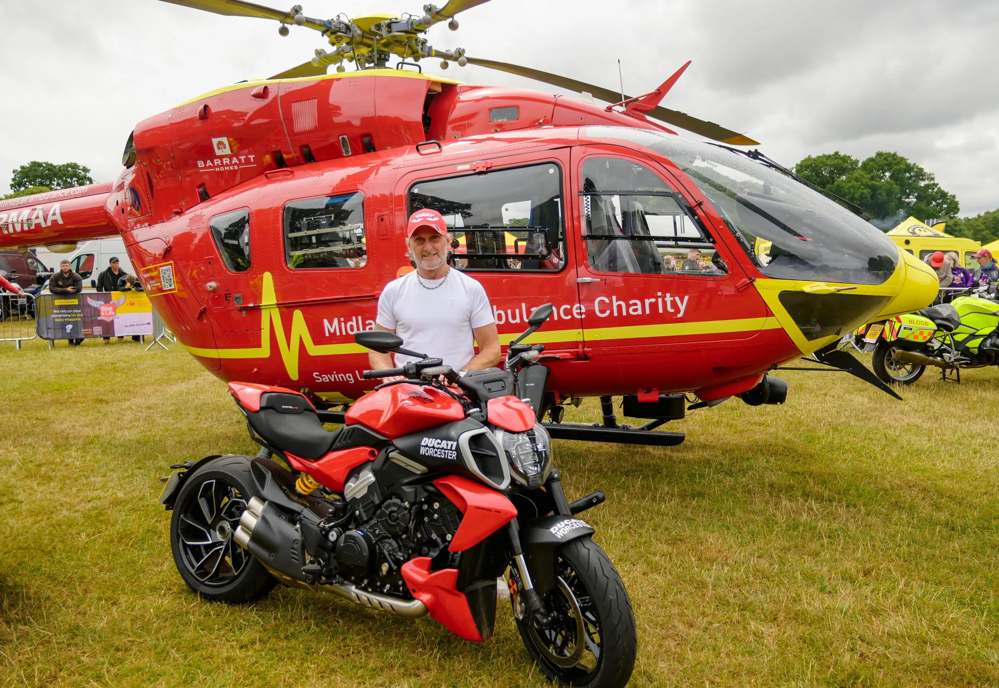 Maac Man Standing Next To A Red Motorcycle In Front Of A Helicopter