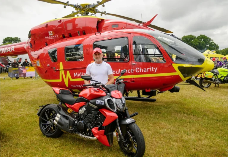 Maac Man Standing Next To A Red Motorcycle In Front Of A Helicopter
