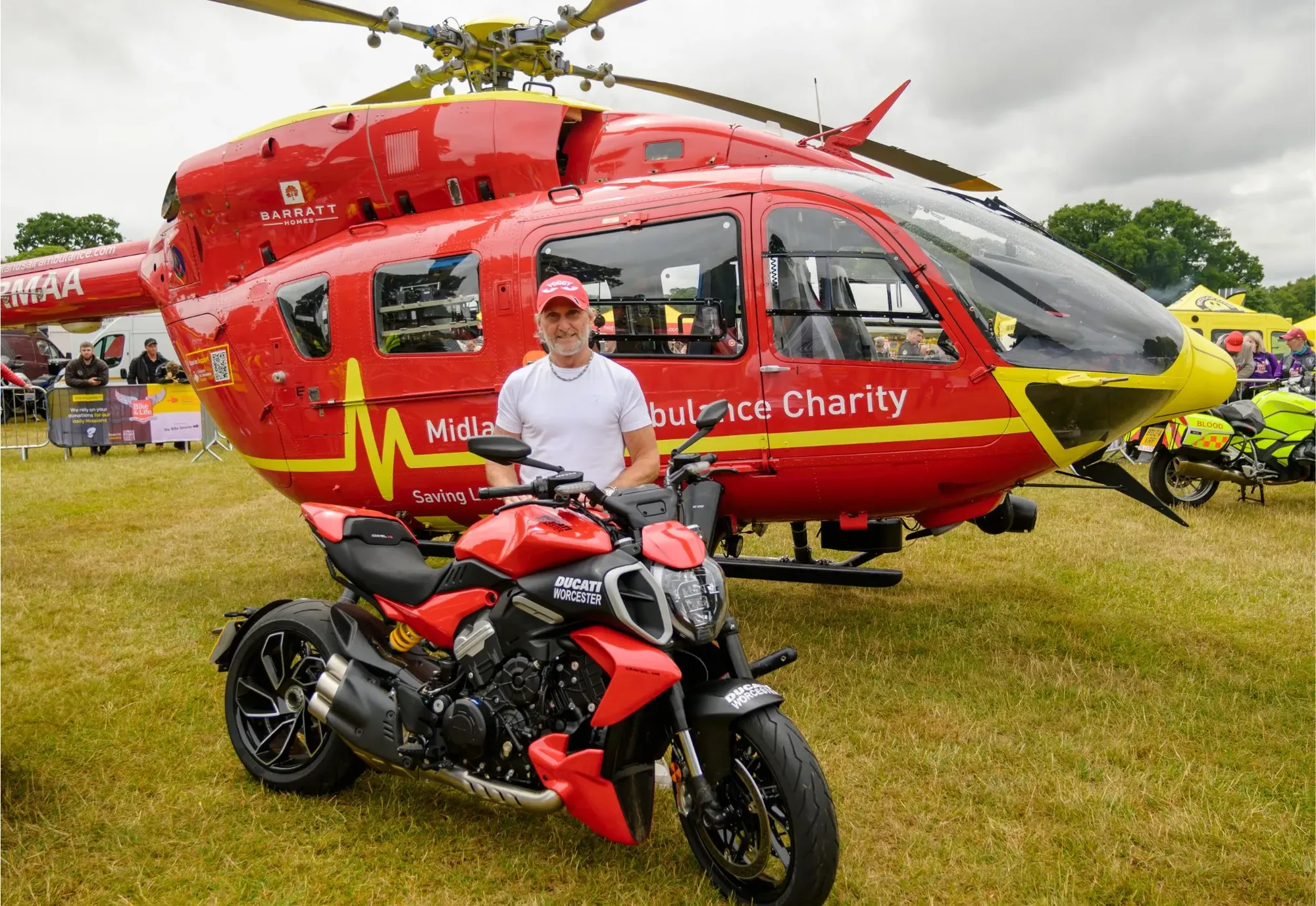 Maac Man Standing Next To A Red Motorcycle In Front Of A Helicopter