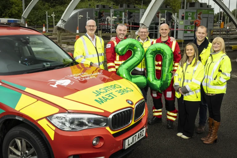 Maac People In Yellow Jackets Standing Next To A Car With A Number Balloon