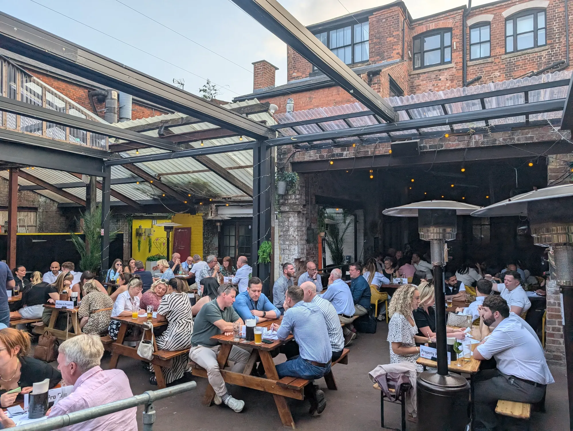 Maac People Sitting At Tables Outside Of A Restaurant With A Lot Of Windows